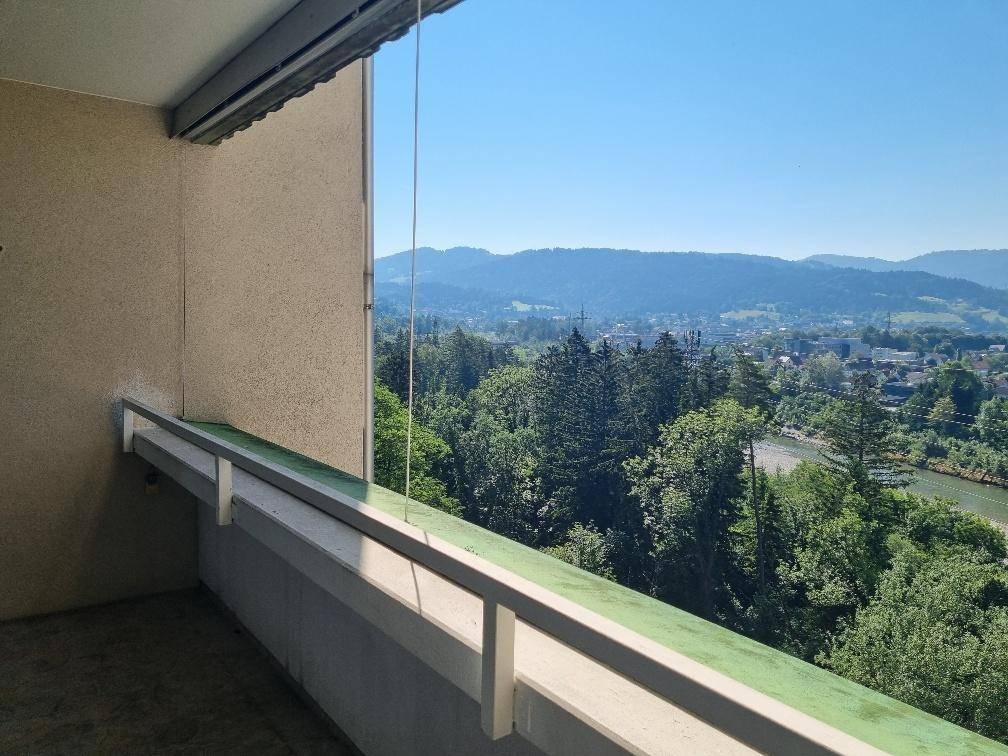 Balkon mit Glasgeländer bietet einen weiten Blick über die grüne Landschaft und Berge.