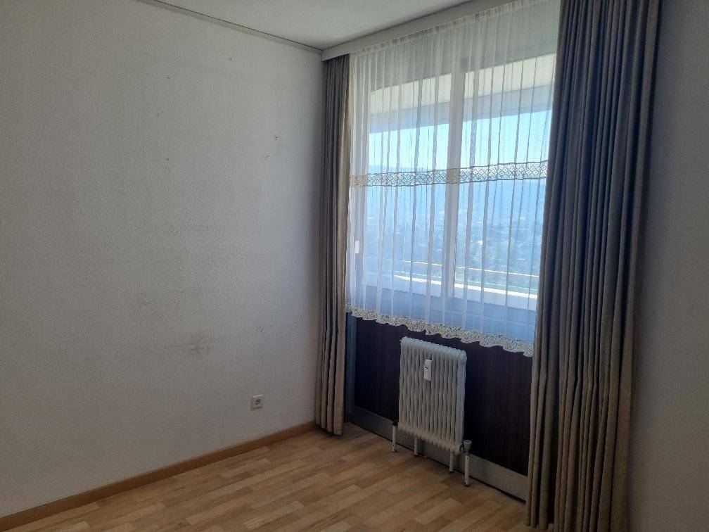 Helles Schlafzimmer mit Parkettboden, großem Fenster und Heizkörper.