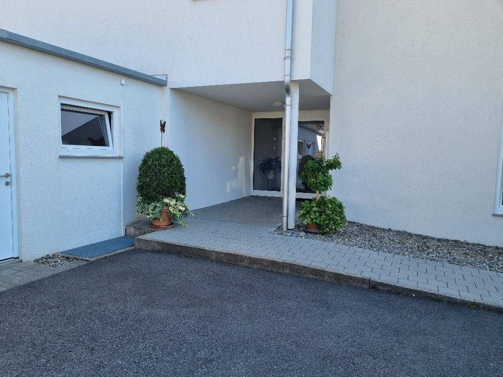 Detailansicht des Gebäudeeingangs mit barrierefreier Rampe und dekorativen Pflanzen.