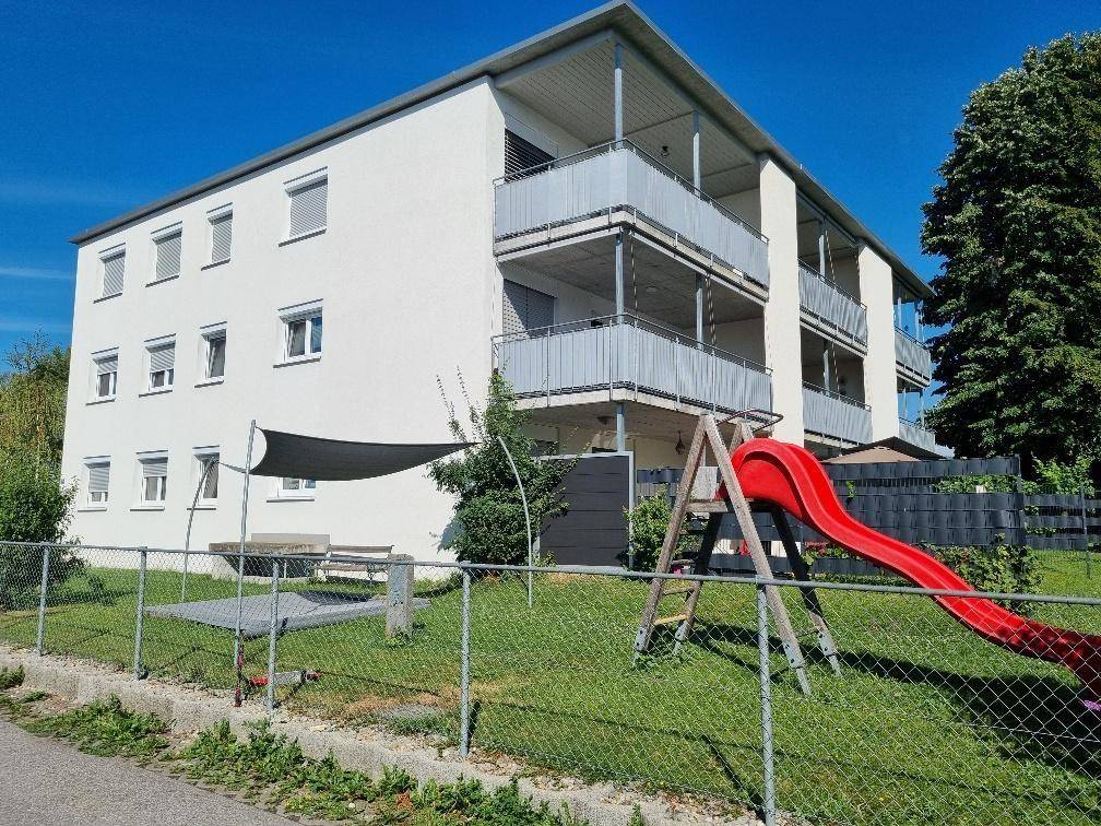 Rückseite eines Wohngebäudes mit Balkonen und einem Spielplatz im gemeinschaftlichen Gartenbereich.