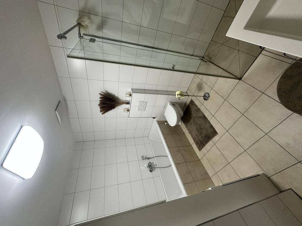 Modernes Badezimmer mit Dusche, Badewanne und hellen Fliesen.