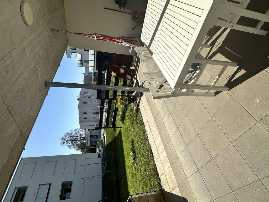 Geräumige Terrasse mit hellen Gartenmöbeln und Blick auf die umliegenden Gebäude.