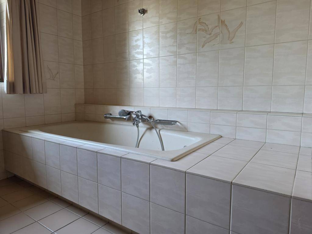 Gefliestes Badezimmer mit einer eingebauten Badewanne und hellen Wandfliesen in neutralen Tönen.