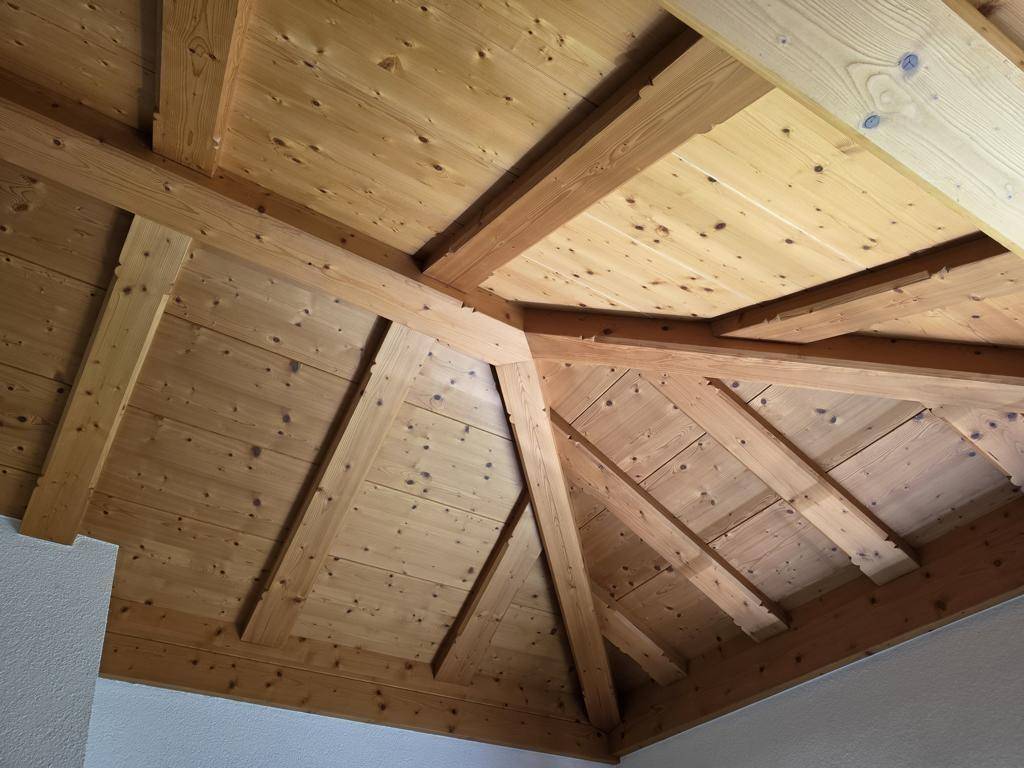 Detailaufnahme einer Holzdecke mit sichtbaren Balken und der Dachkonstruktion, die eine warme Atmosphäre schafft.