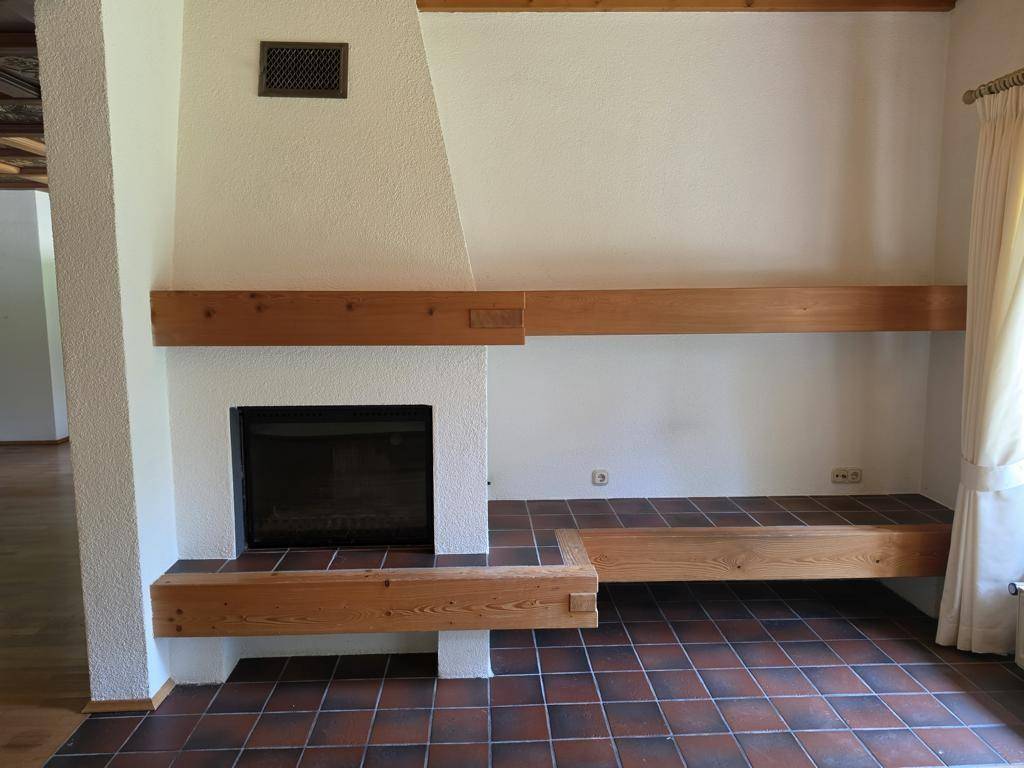 Gemütlicher Kaminbereich mit Holzelementen und Fliesenboden im Wohnzimmer, ideal für kalte Tage.