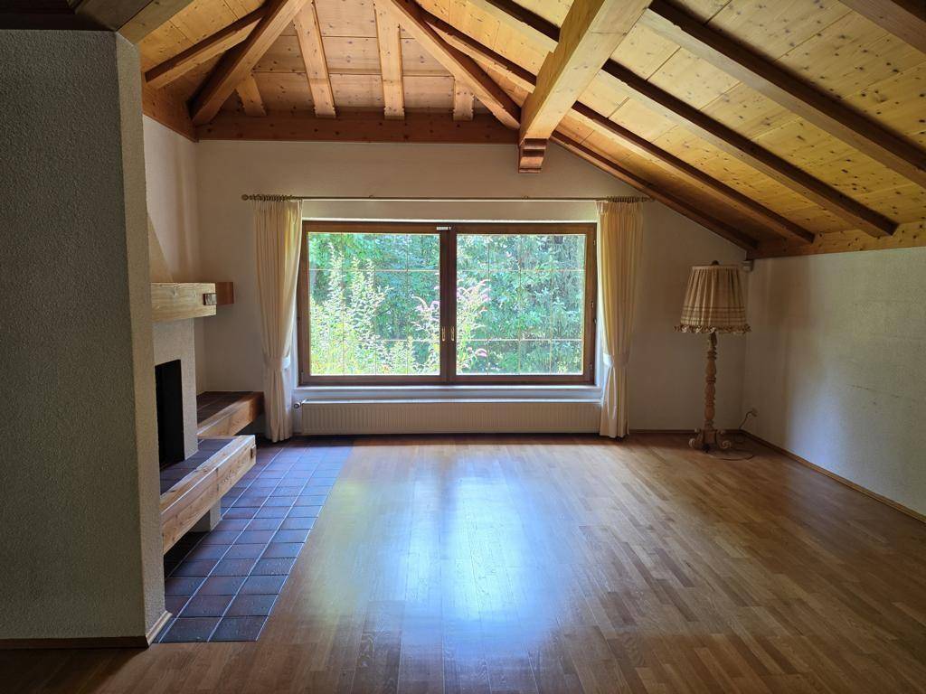 Helles Wohnzimmer mit Holzboden, großem Fenster und sichtbaren Dachbalken, die Charakter verleihen.