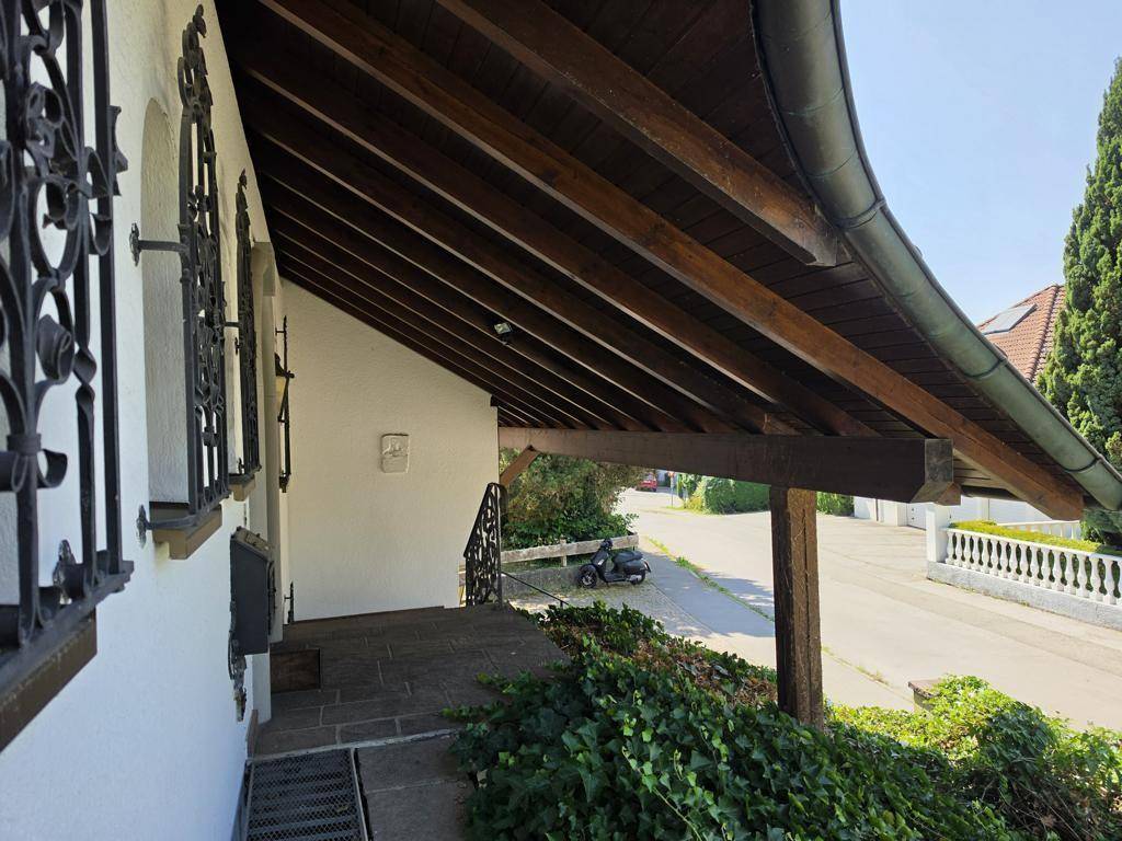 Überdachter Eingangsbereich mit Holzbalken, Steinfliesen und schmiedeeisernen Fenstergittern im traditionellen Stil.