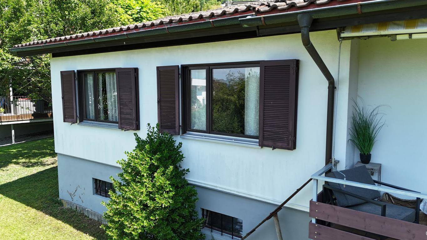 Helles Arbeitszimmer mit großem Fenster, modernem Sessel und dunklen Wänden.