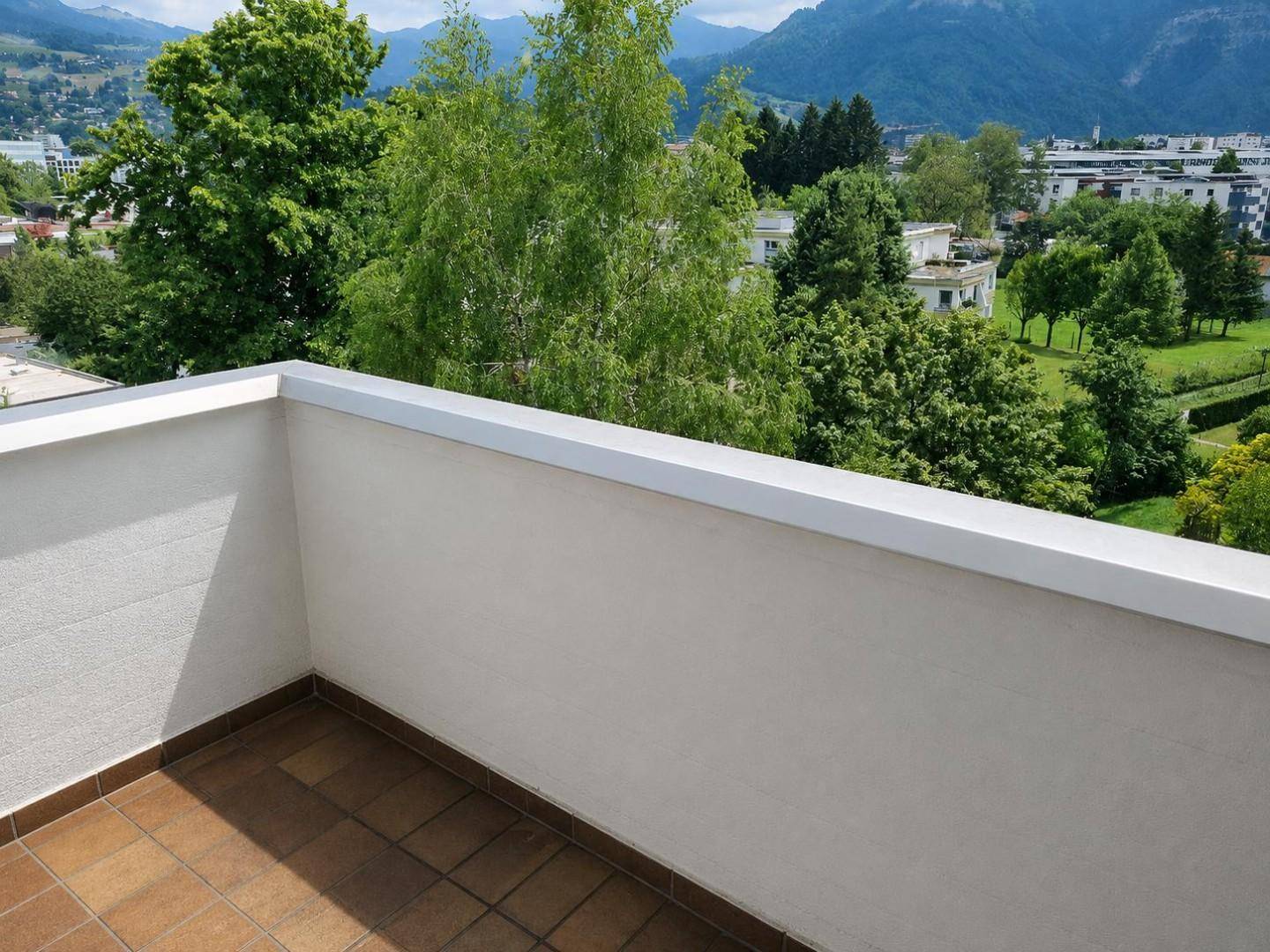 Balkon mit Fliesenboden und weitem Blick ins Grüne sowie auf die umliegenden Berge.