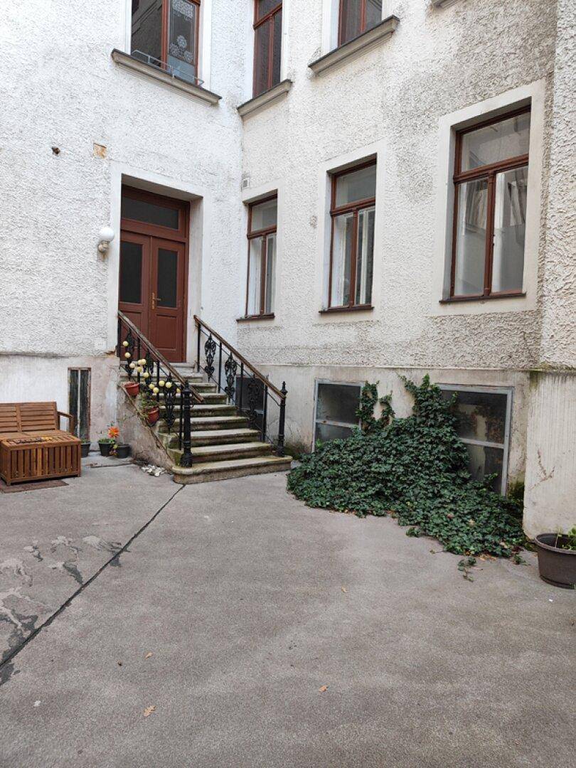 Innenhof mit Außentreppe, die zu einem Eingang führt, und begrünten Bereichen.