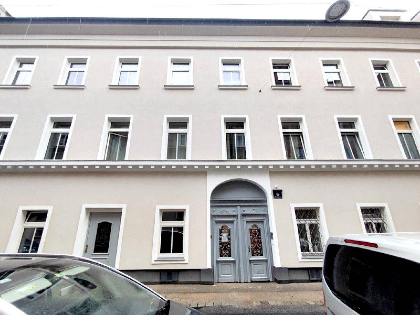 Klassische Fassade eines Mehrfamilienhauses mit traditionellen Fenstern und einer verzierten Eingangstür.