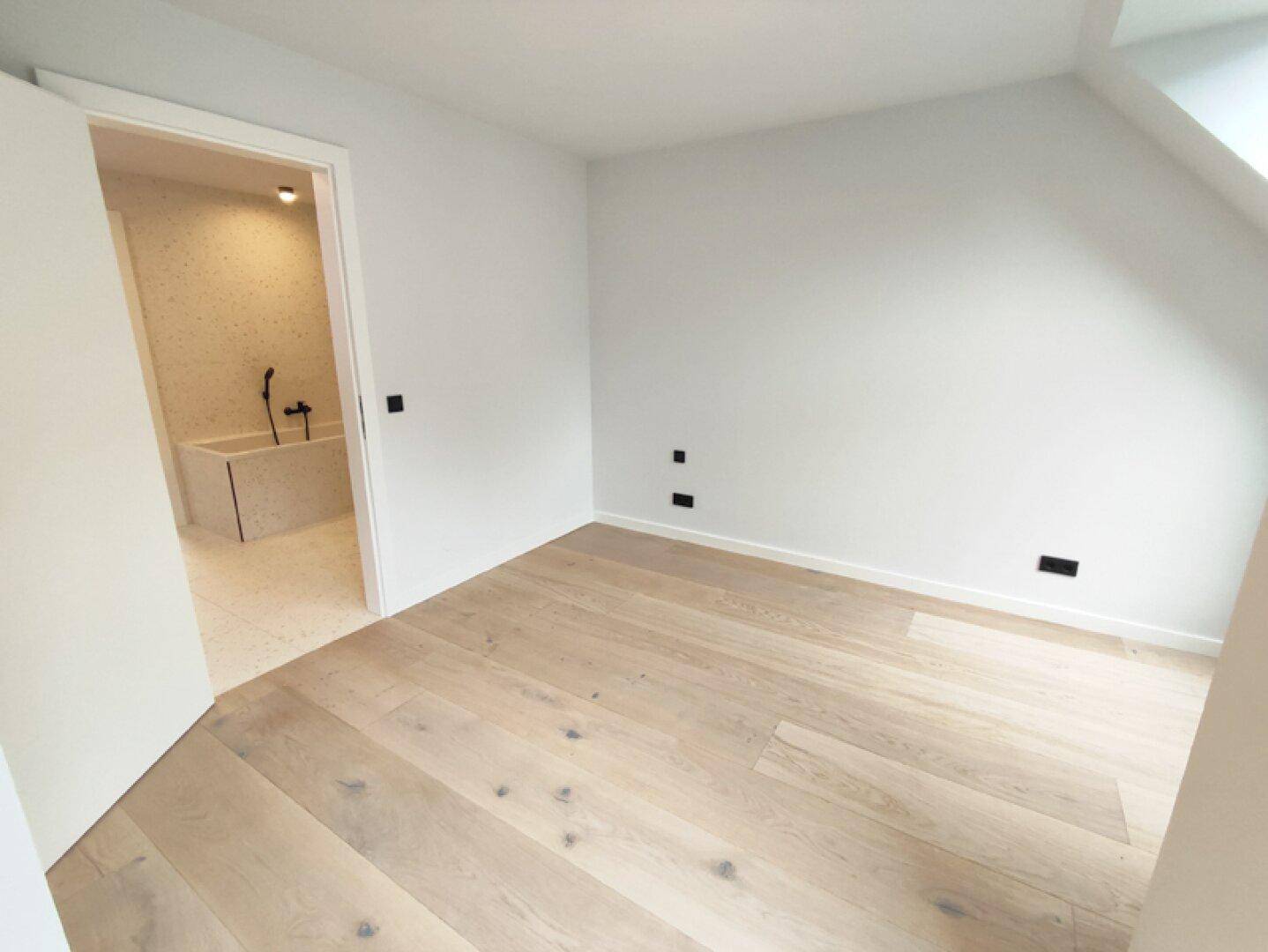 Helles Schlafzimmer mit Holzboden und direktem Zugang zu einem modernen Badezimmer.