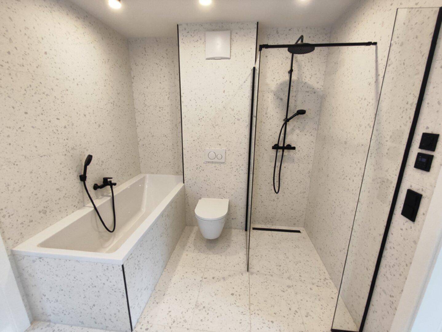 Elegantes Badezimmer mit Badewanne, bodengleicher Dusche und modernen Fliesen in Terrazzo-Optik.