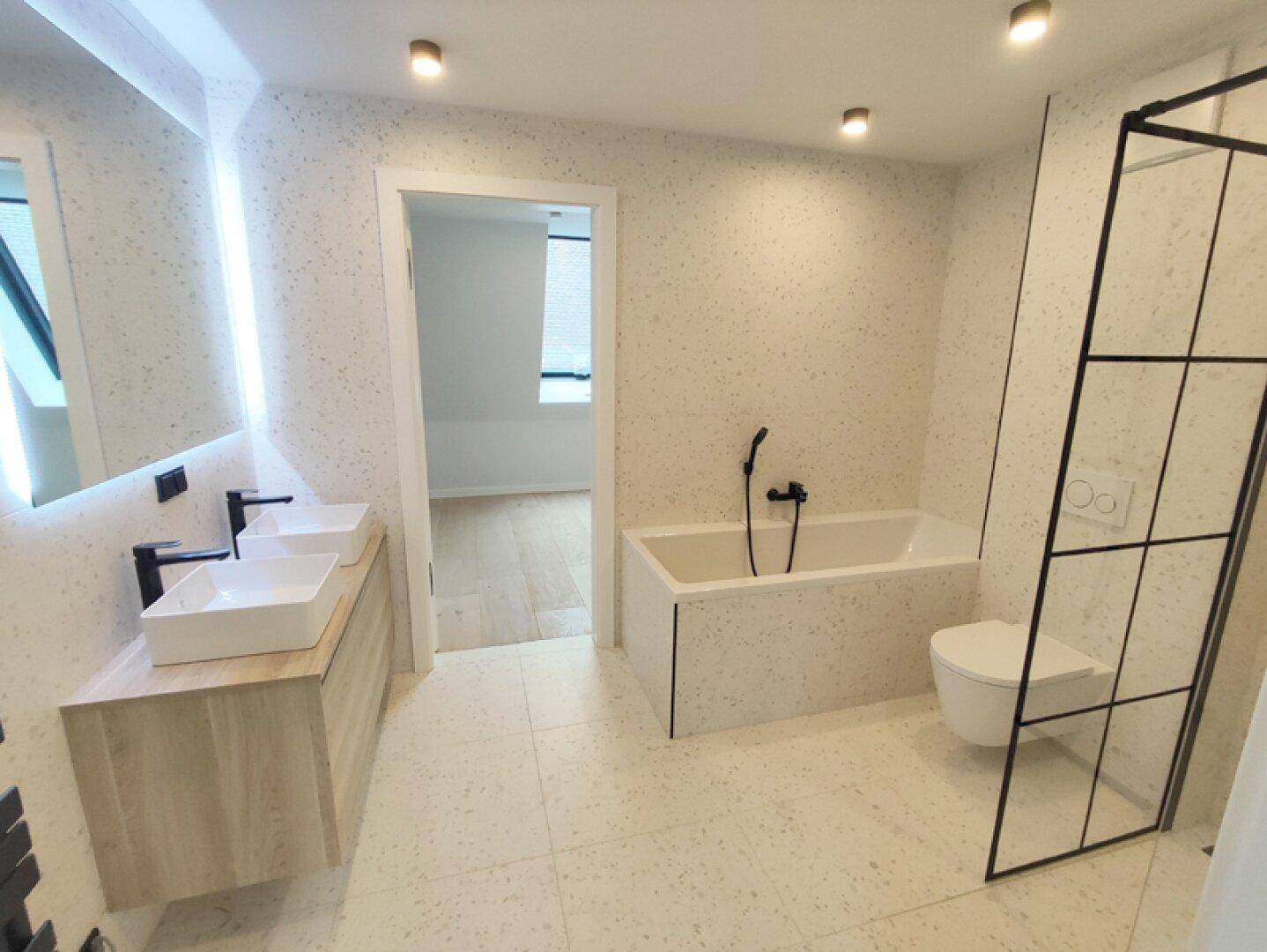 Modernes Badezimmer mit Doppelwaschbecken, Badewanne und Duschbereich in Terrazzo-Optik.