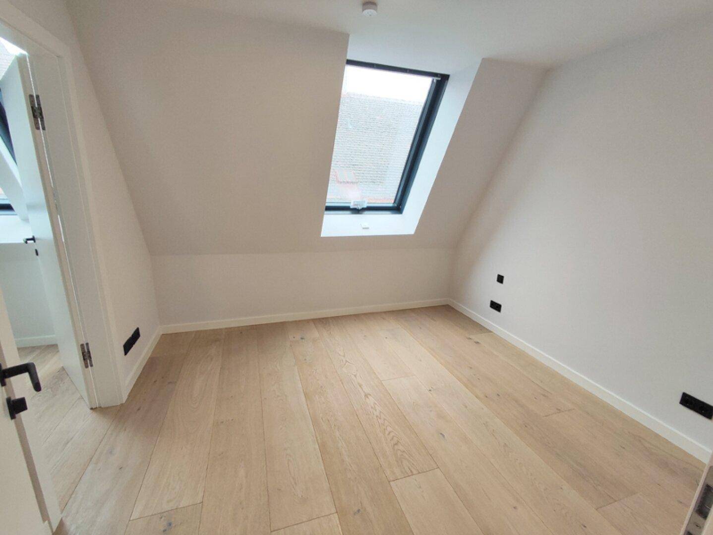 Helles Schlafzimmer im Dachgeschoss mit Holzboden und großem Dachfenster für viel Tageslicht.