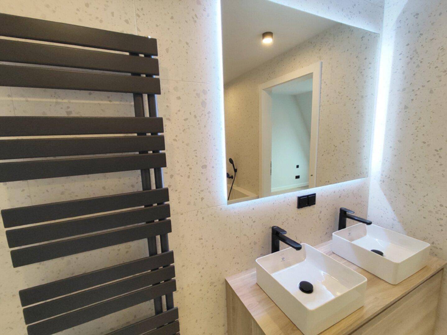 Modernes Badezimmer mit Doppelwaschbecken, beleuchtetem Spiegel und beheiztem Handtuchhalter.