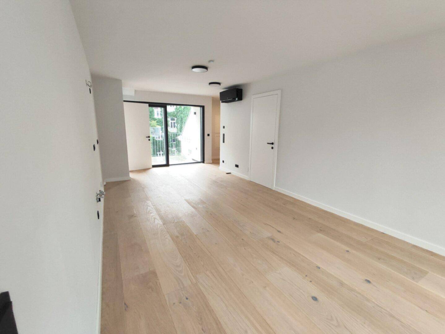 Heller, leerer Wohnraum mit modernem Holzparkett und großzügigem Zugang zu einem Balkon.