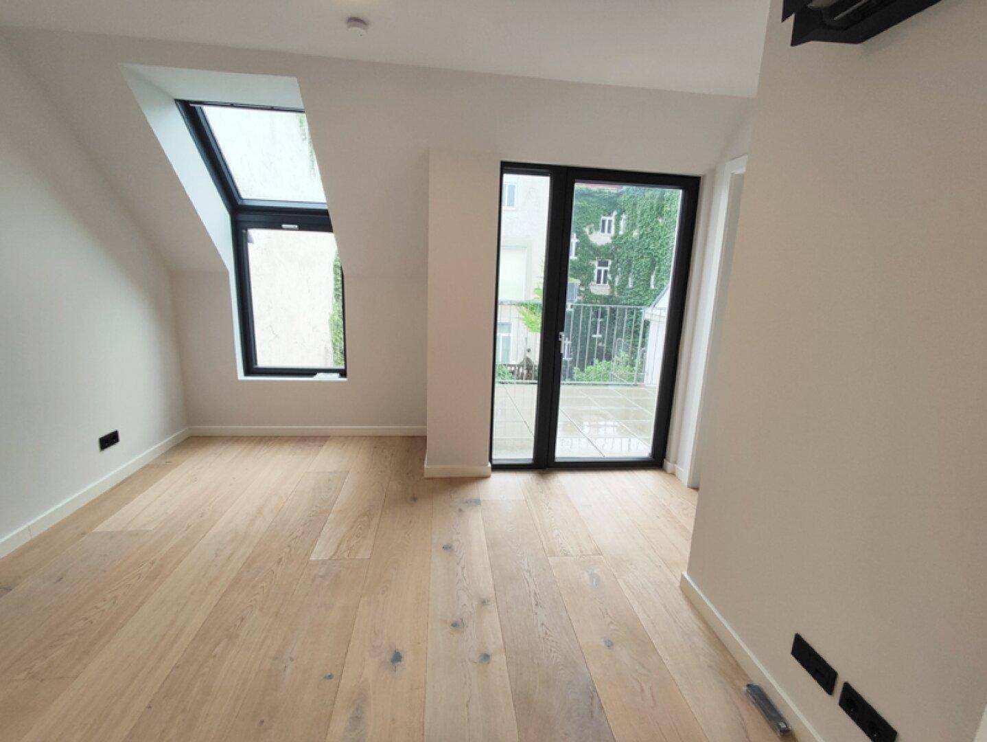 Helles Schlafzimmer im Dachgeschoss mit Holzboden, Dachfenster und Balkonzugang.