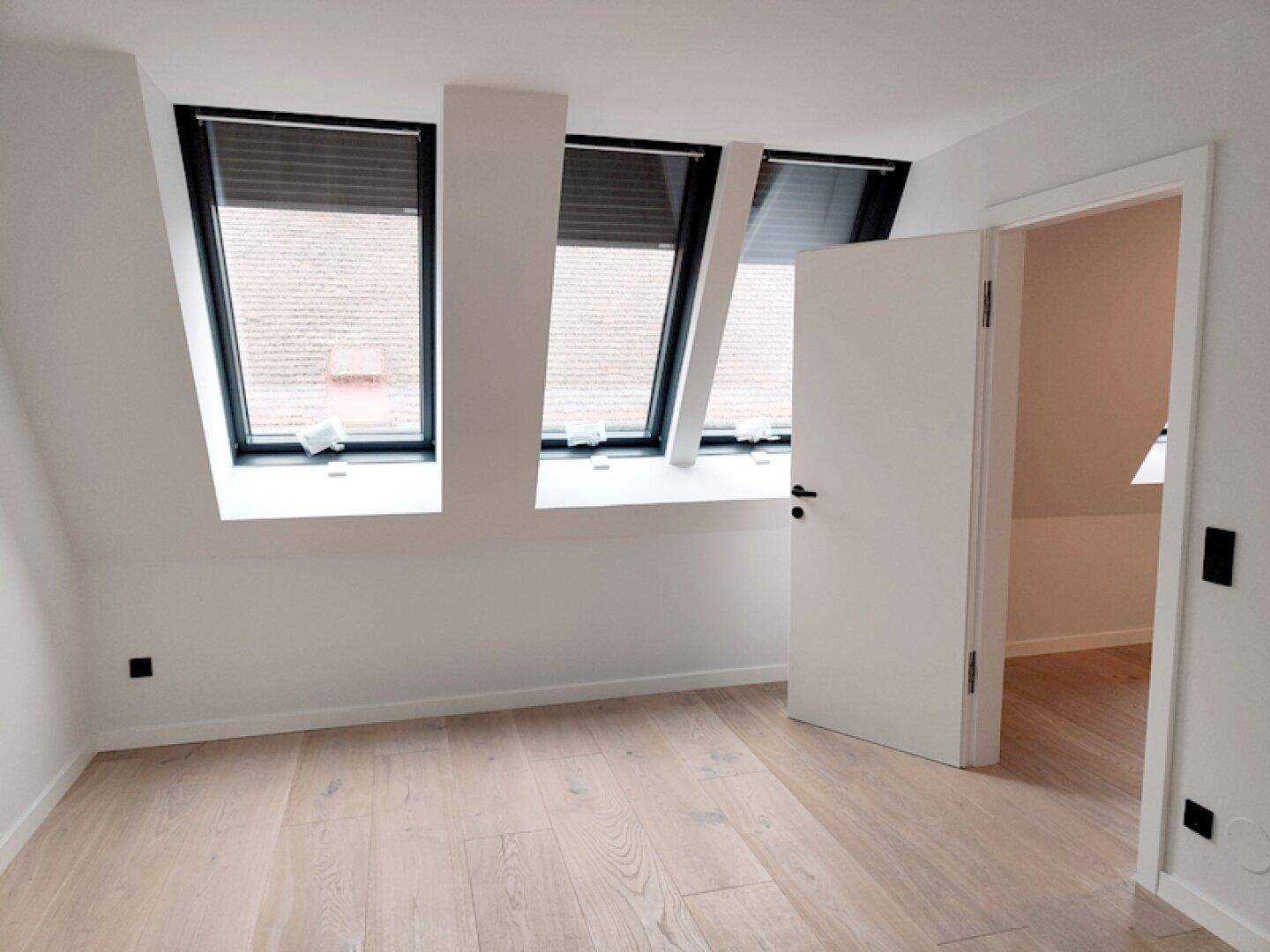 Helles Schlafzimmer im Dachgeschoss mit Holzboden und mehreren Dachfenstern für optimale Belichtung.