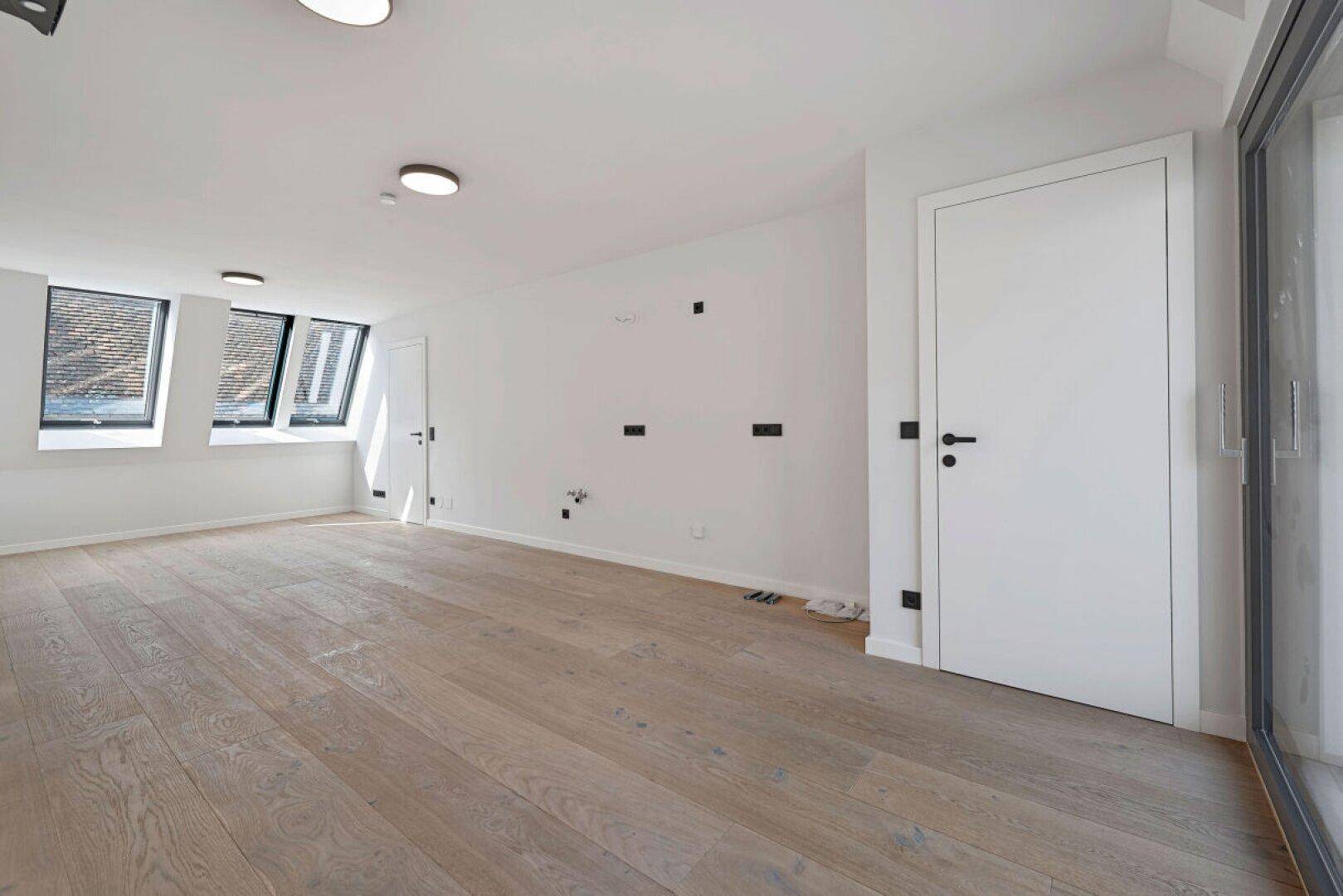 Geräumiger, heller Wohnbereich mit Holzboden und mehreren Fenstern im Dachgeschoss.