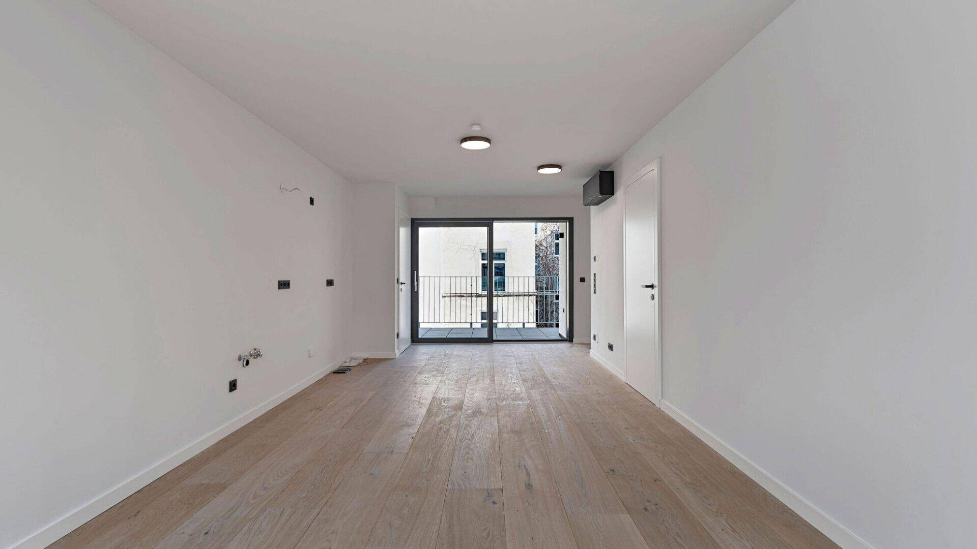 Geräumiger, heller Wohnbereich mit Holzboden und Zugang zu einem französischen Balkon.