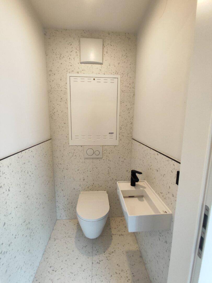 Modernes Gäste-WC mit wandhängender Toilette und kleinem Waschbecken in Terrazzo-Optik.