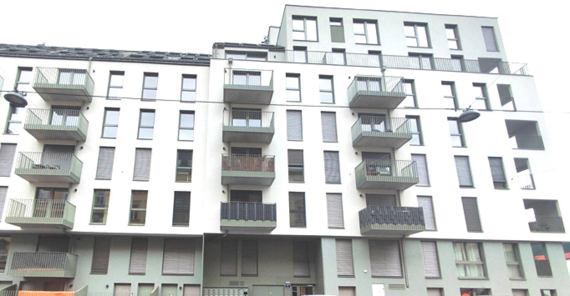 Moderne Wohnhausfassade mit zahlreichen Balkonen und großen Fenstern in städtischer Umgebung.