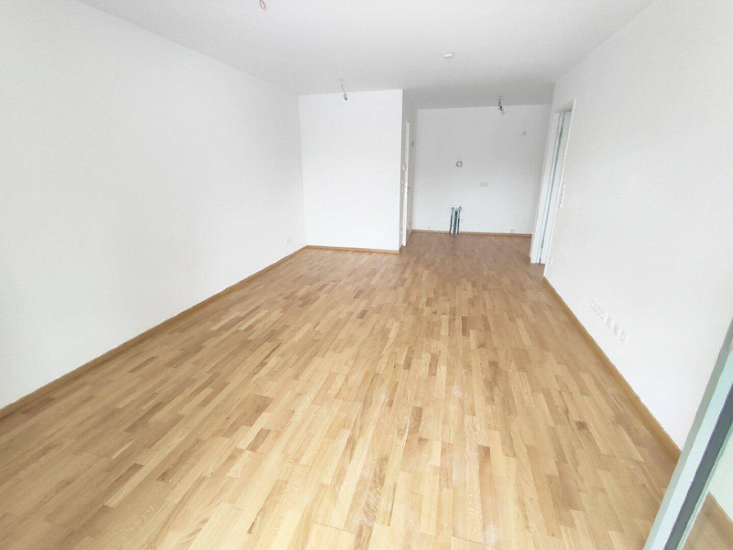 Geräumiger, unmöblierter Raum mit hellem Parkettboden und weißen Wänden, bereit zum Einzug.