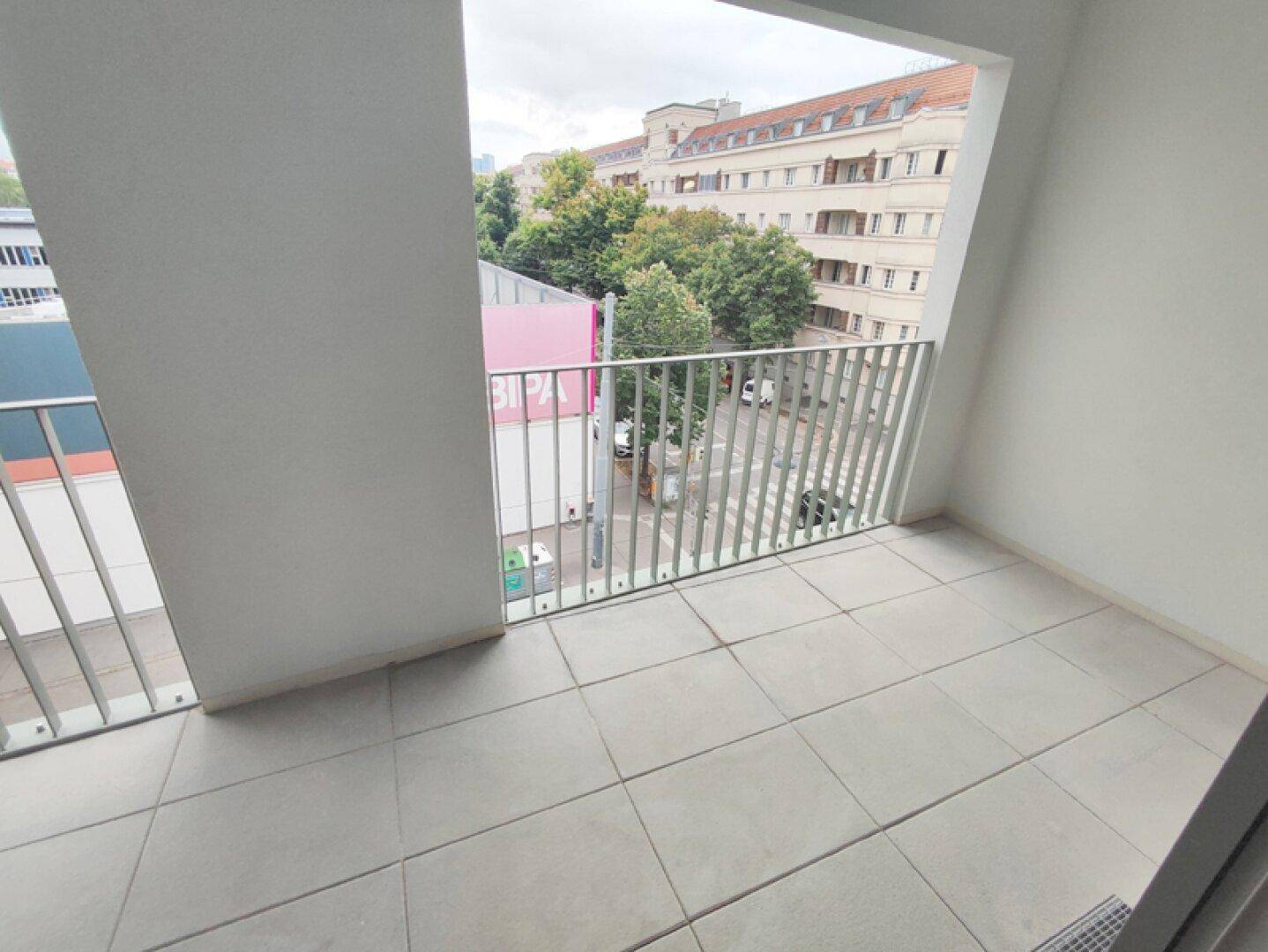 Gefliester Balkon mit Metallgeländer und Blick auf die städtische Umgebung mit Bäumen.