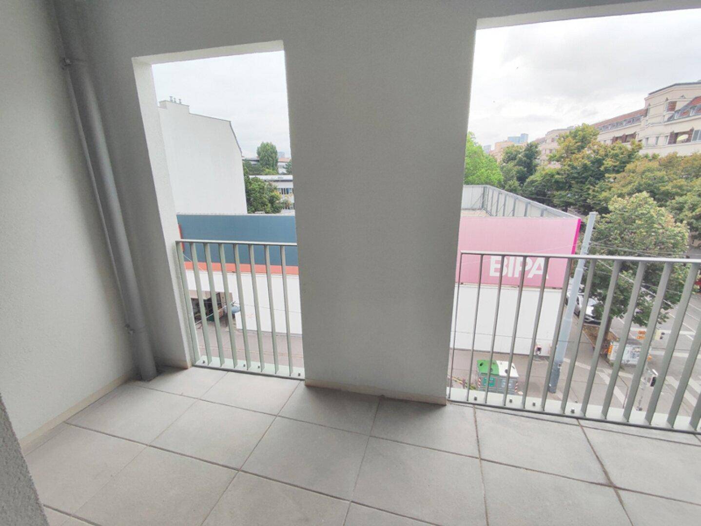 Balkon mit Fliesenboden und modernem Geländer, bietet einen Ausblick auf die Stadt.