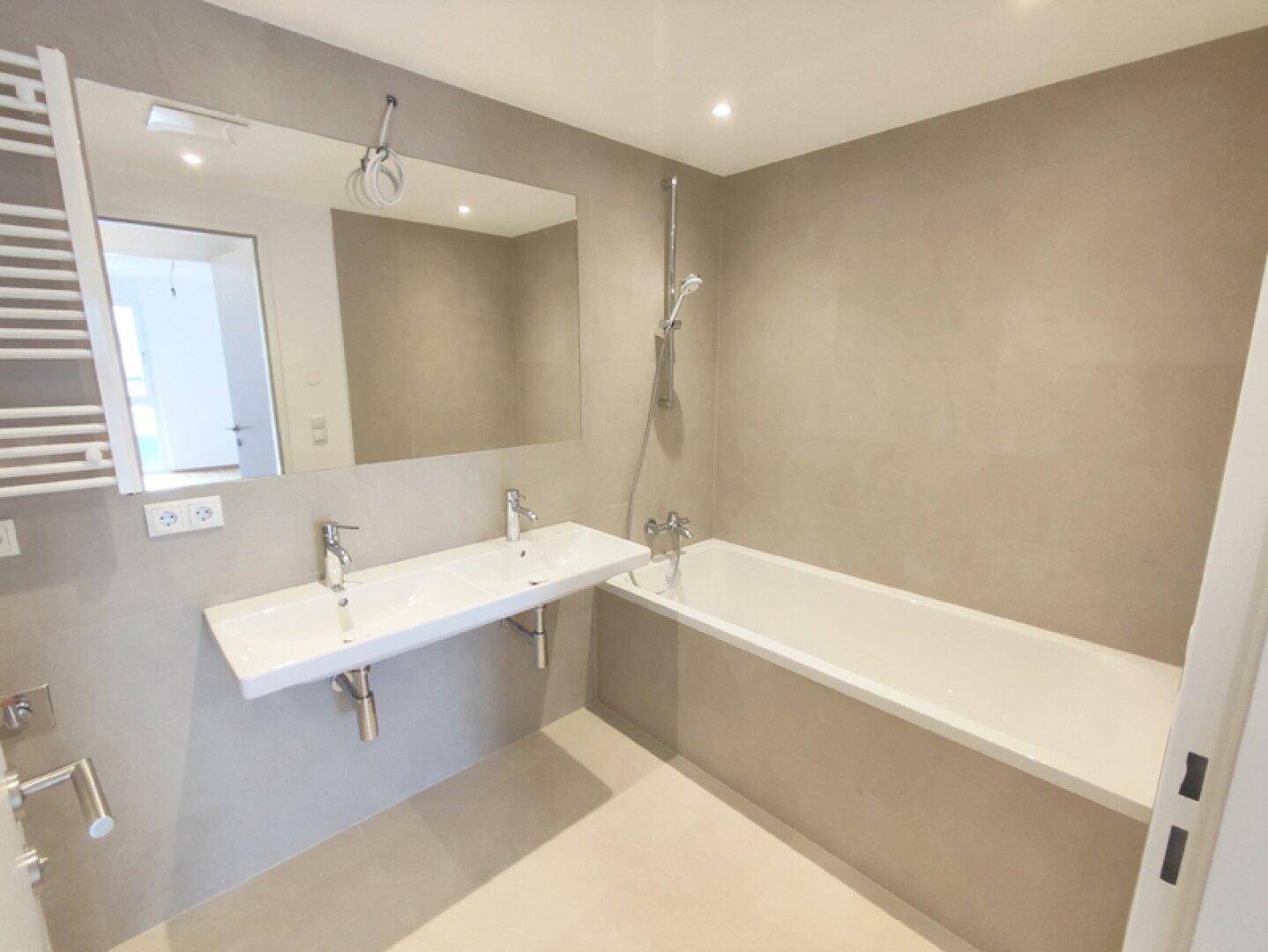 Modernes Badezimmer mit Doppelwaschbecken, Badewanne und beheiztem Handtuchhalter.