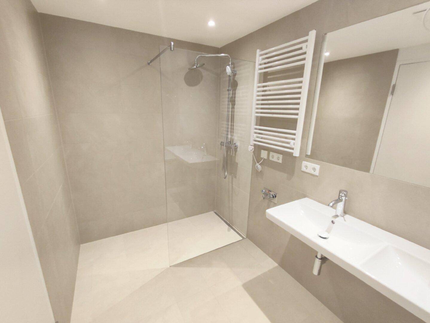 Modernes Badezimmer mit ebenerdiger Dusche, Einzelwaschbecken und beheiztem Handtuchhalter.