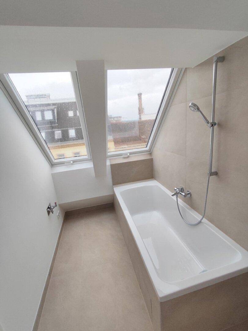 Modernes Badezimmer mit Badewanne und Dachfenstern, die den Raum mit Licht füllen.