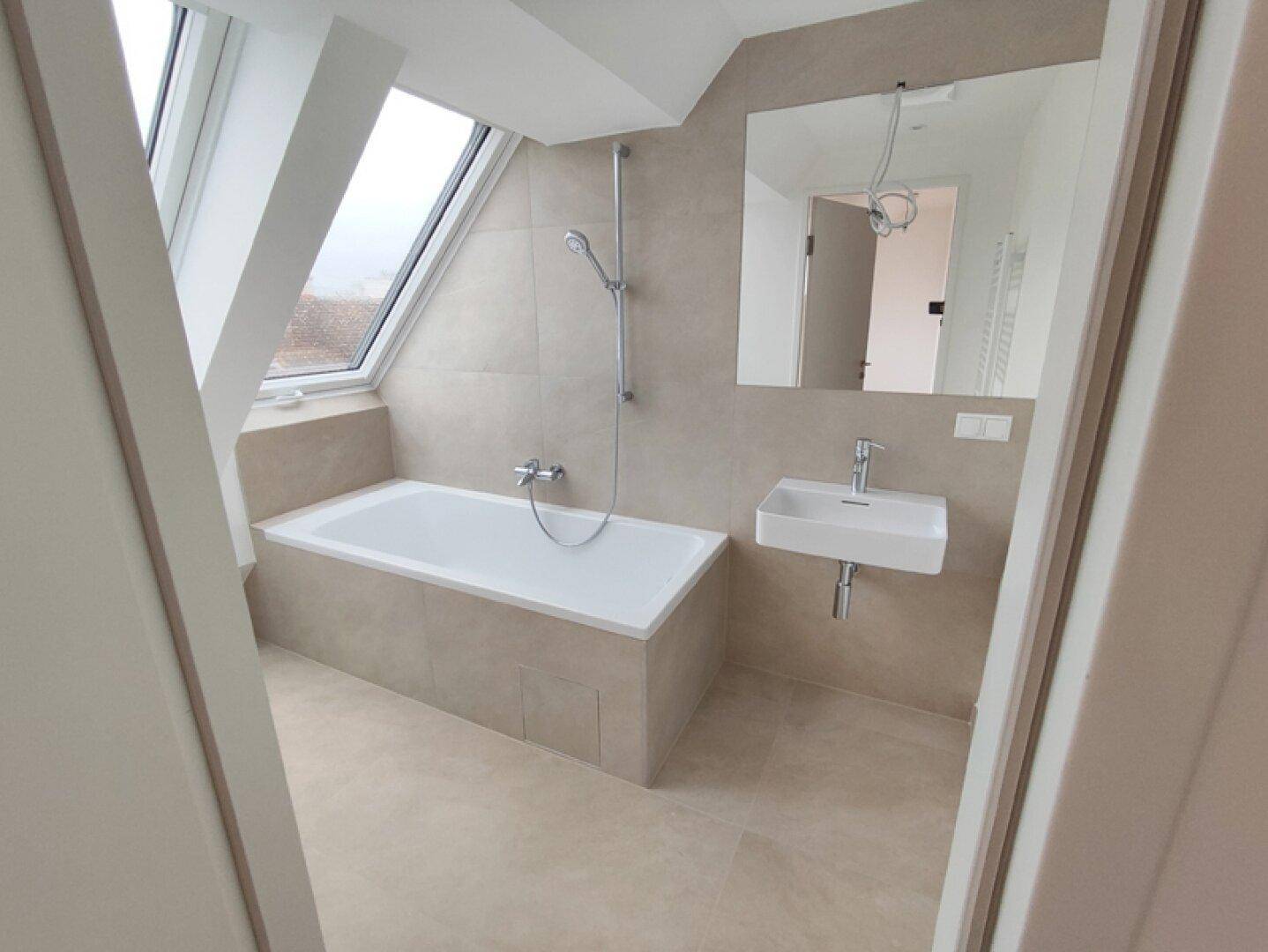 Modernes Badezimmer mit Badewanne, Waschbecken und Dachfenster unter einer Dachschräge.