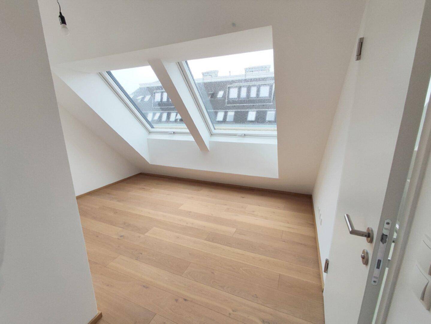 Helles Zimmer im Dachgeschoss mit Holzboden und großen Dachfenstern, ideal als Schlafzimmer.