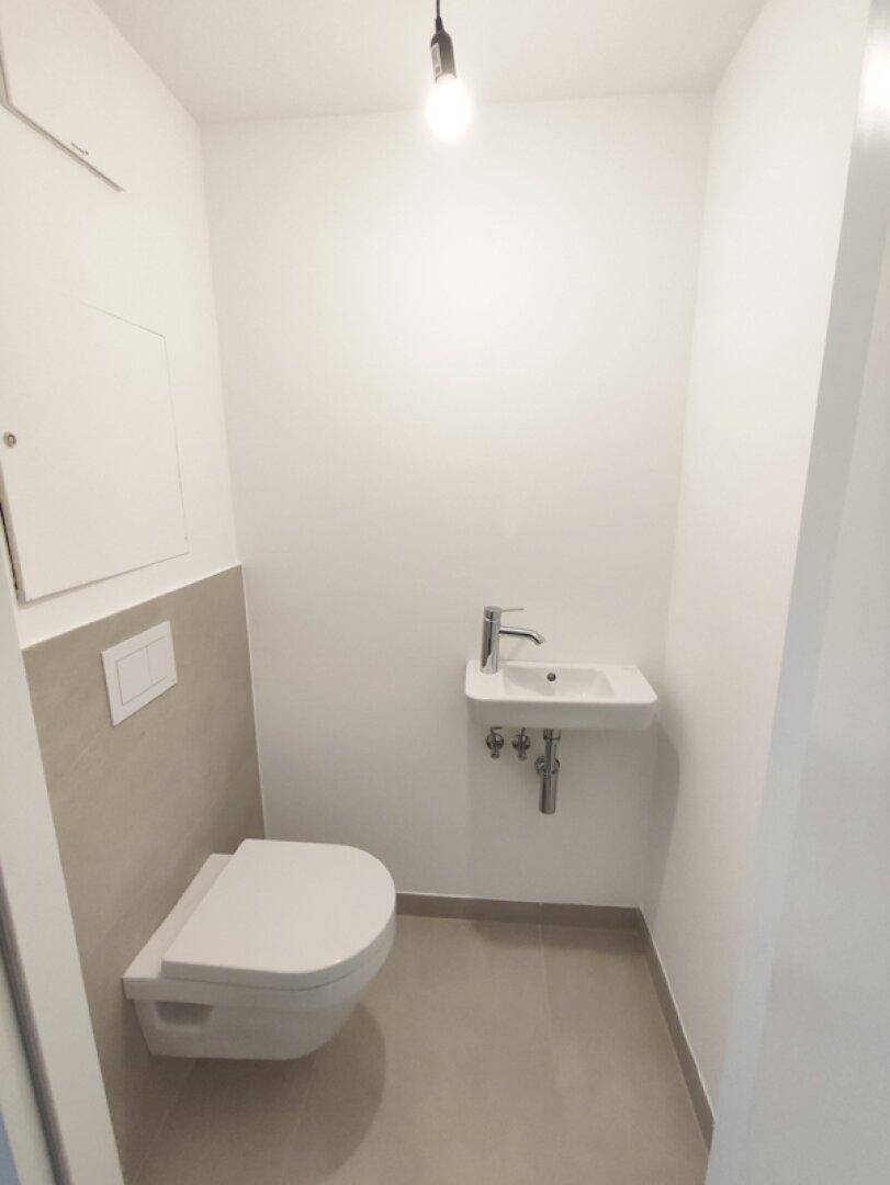 Modernes Gäste-WC mit wandhängender Toilette und kleinem Waschbecken.