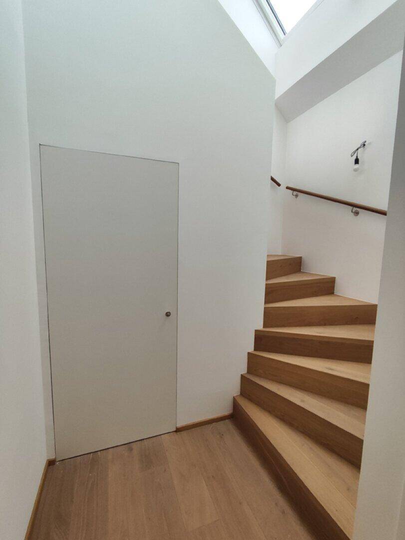 Heller Treppenaufgang mit Holzstufen und einem unauffälligen, in die Wand integrierten Tür.