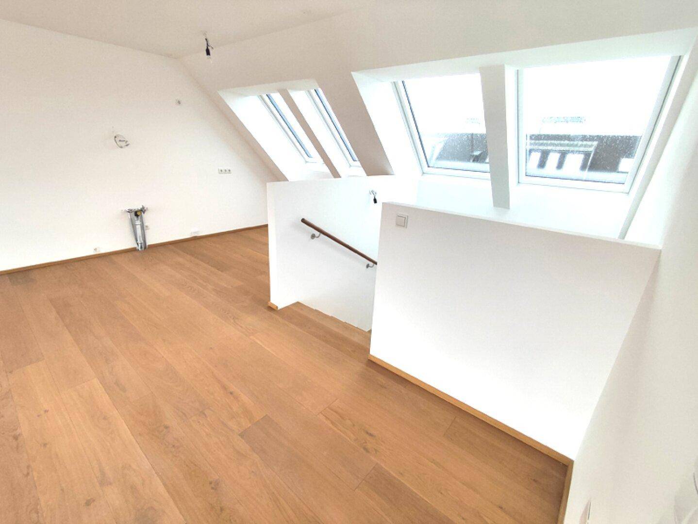 Offener Wohnbereich im Dachgeschoss mit Holzboden, Dachfenstern und Treppenzugang.
