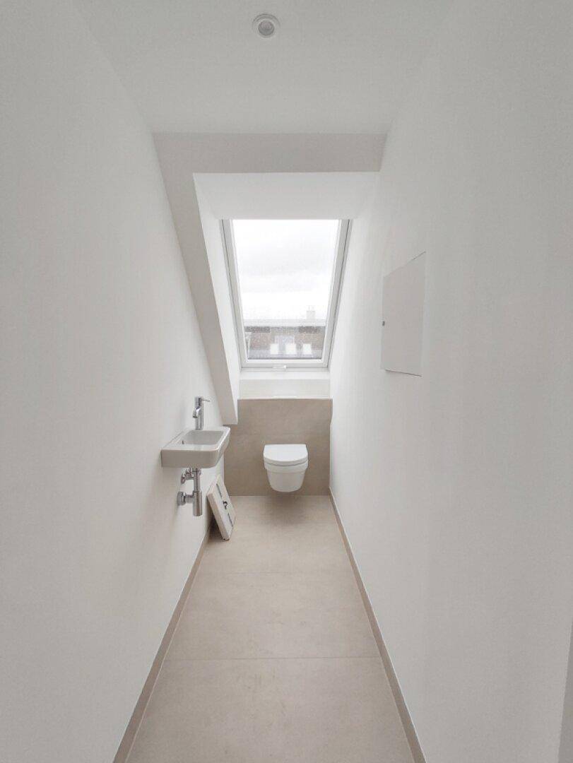 Helles Gäste-WC mit wandhängender Toilette, Waschbecken und einem Dachfenster.