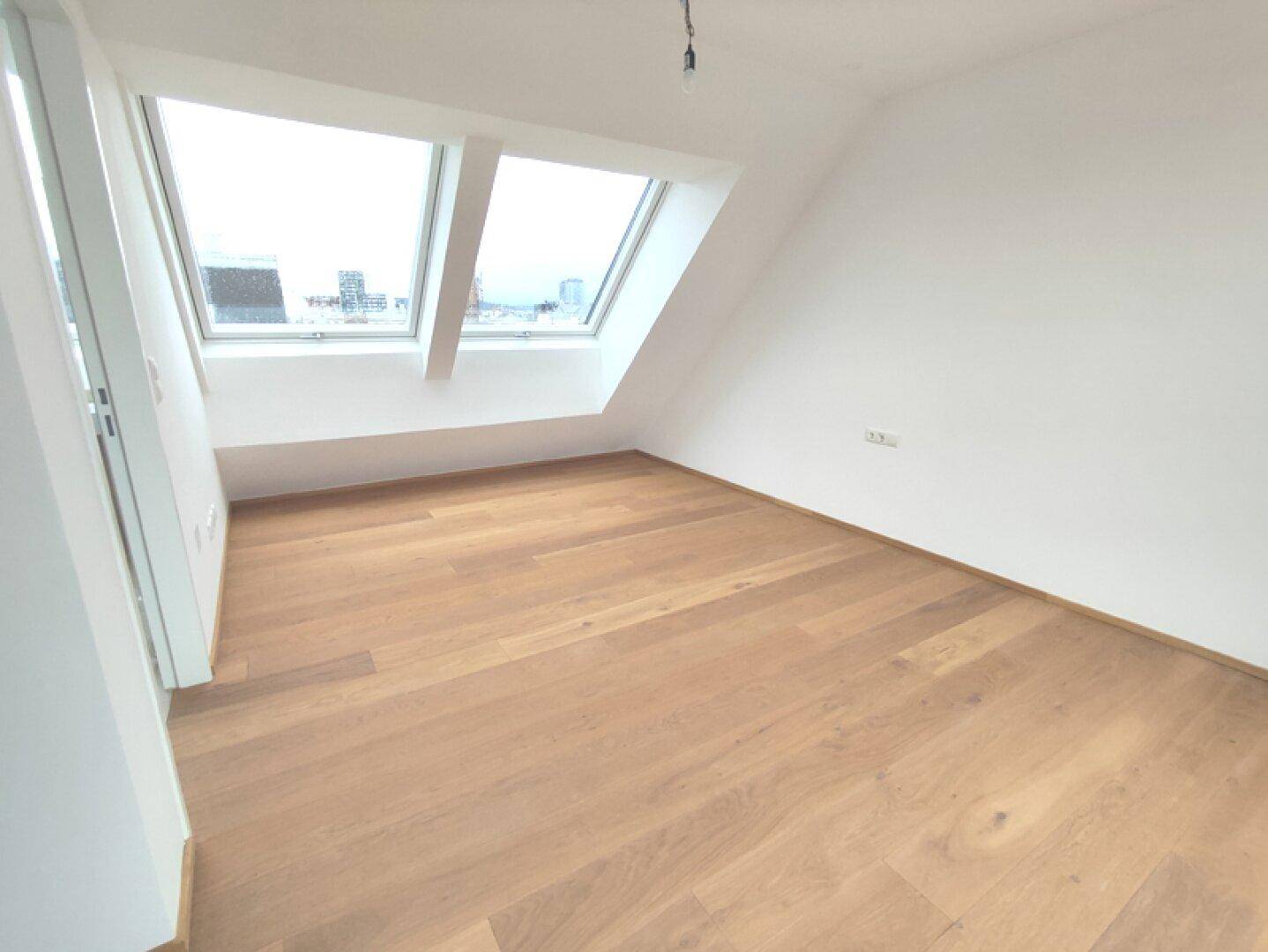 Gemütliches Schlafzimmer im Dachgeschoss mit Holzboden und zwei großen Dachfenstern.