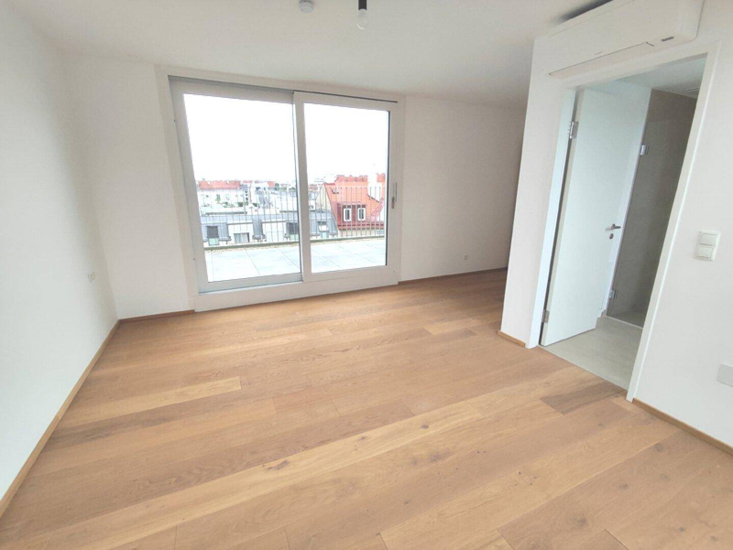 Helles Schlafzimmer mit Holzboden, Klimaanlage und Zugang zu einem Badezimmer.