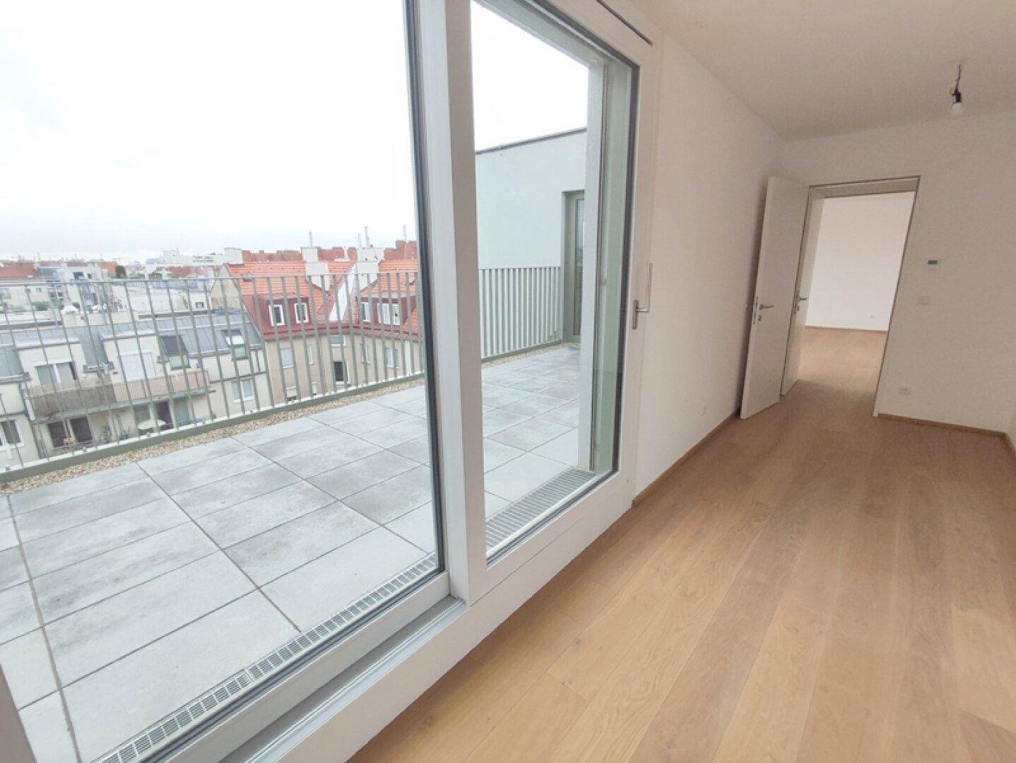 Heller Innenraum mit großen Schiebetüren, die auf eine geräumige Terrasse führen und Stadtblick bieten.