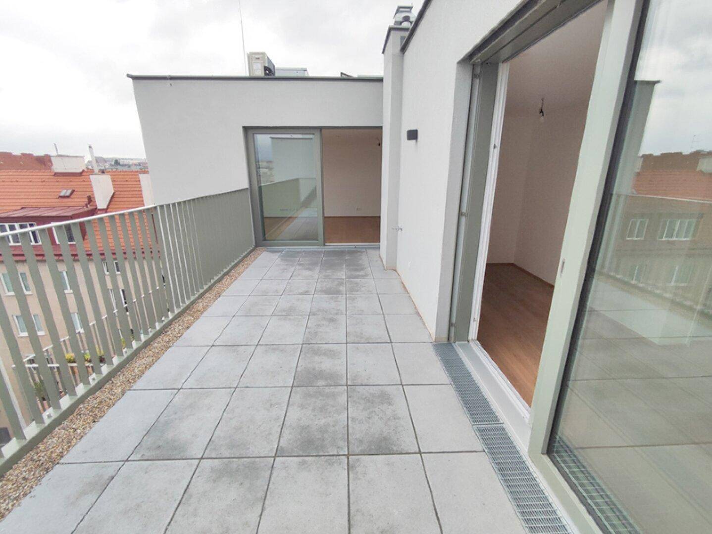 Geräumige Dachterrasse mit Fliesenboden und Blick auf die umliegenden Gebäude.