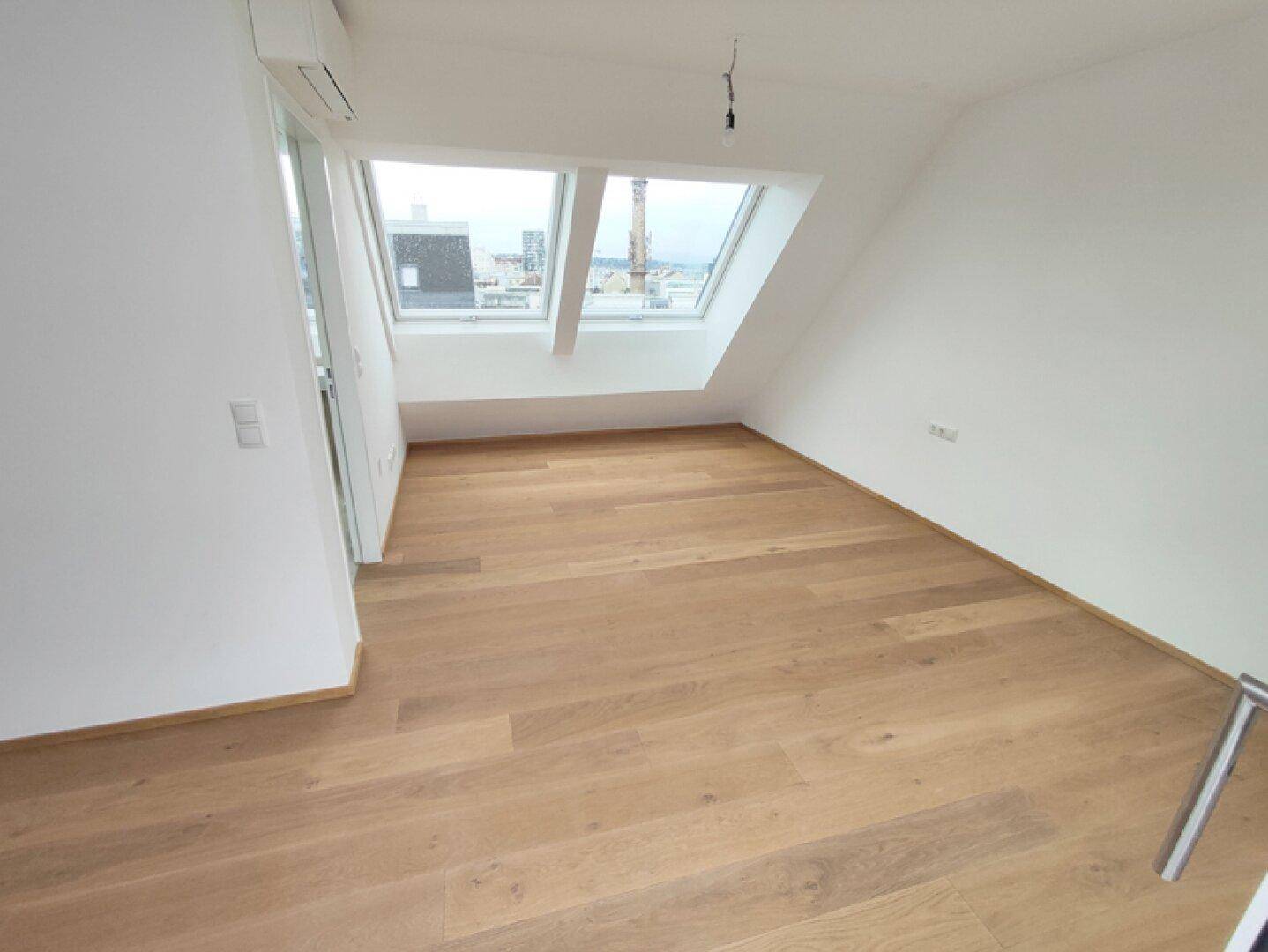 Helles Schlafzimmer im Dachgeschoss mit Holzboden, Klimaanlage und zwei Dachfenstern.