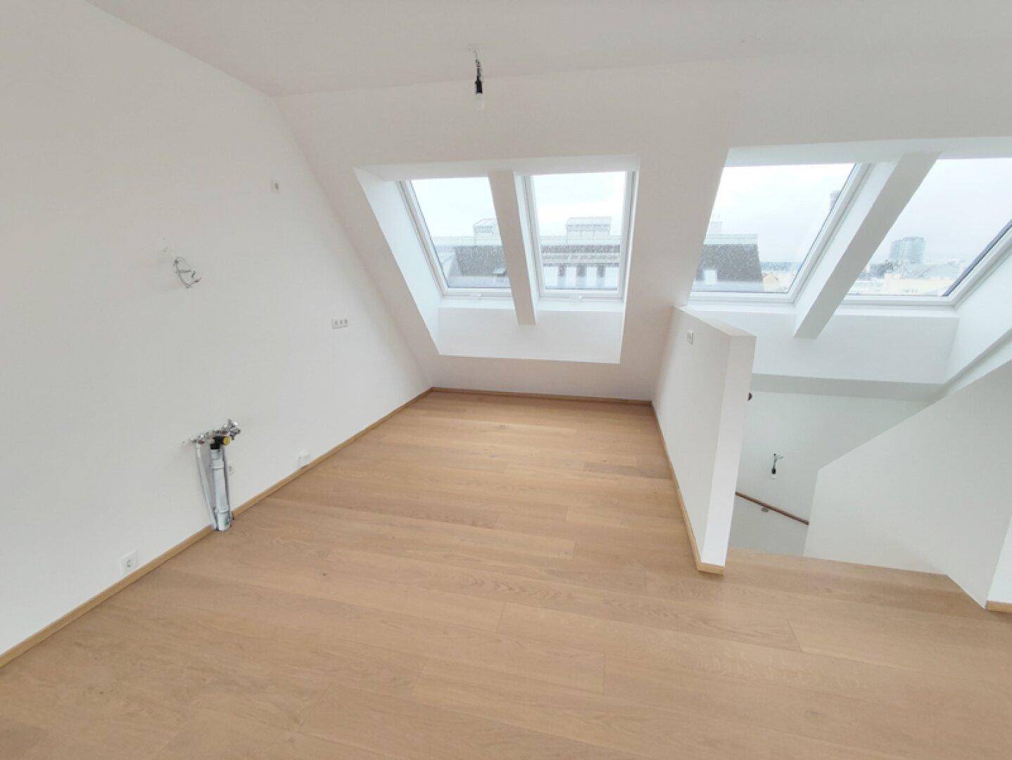 Offener Wohnbereich im Dachgeschoss mit Holzboden, Dachfenstern und Treppenzugang.