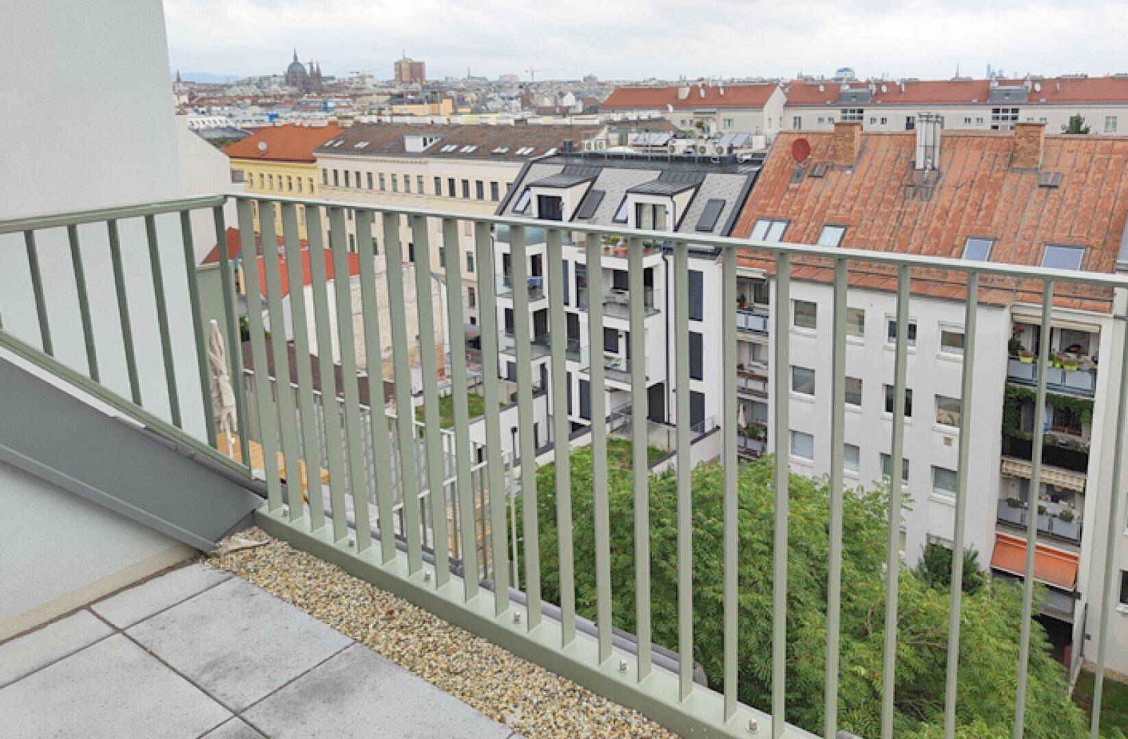 Dachterrasse mit Blick auf die Stadt und die umliegenden Gebäude, umgeben von Grün.