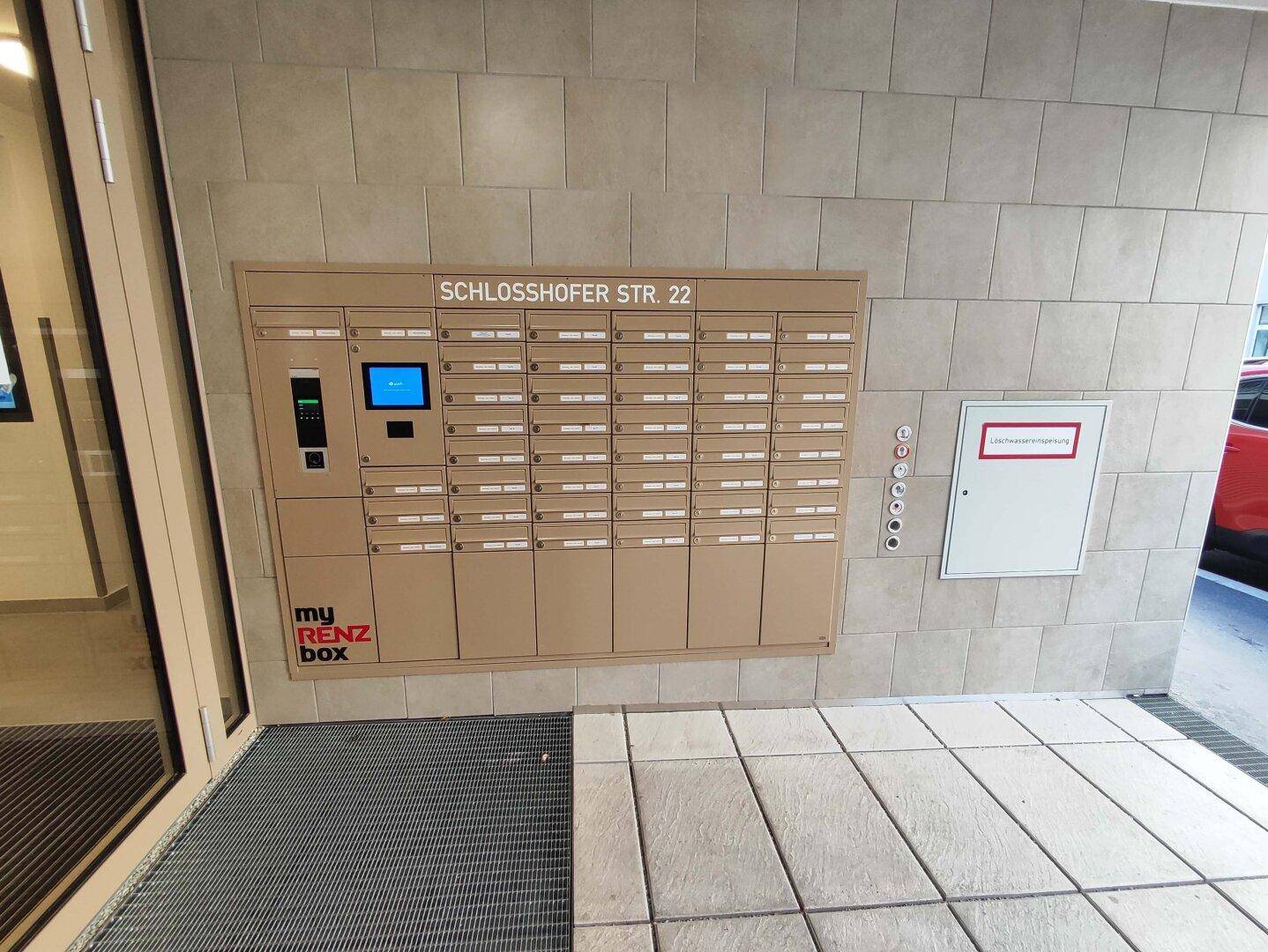 Moderner Eingangsbereich mit Briefkastenanlage und Gegensprechanlage in neutralen Farbtönen.