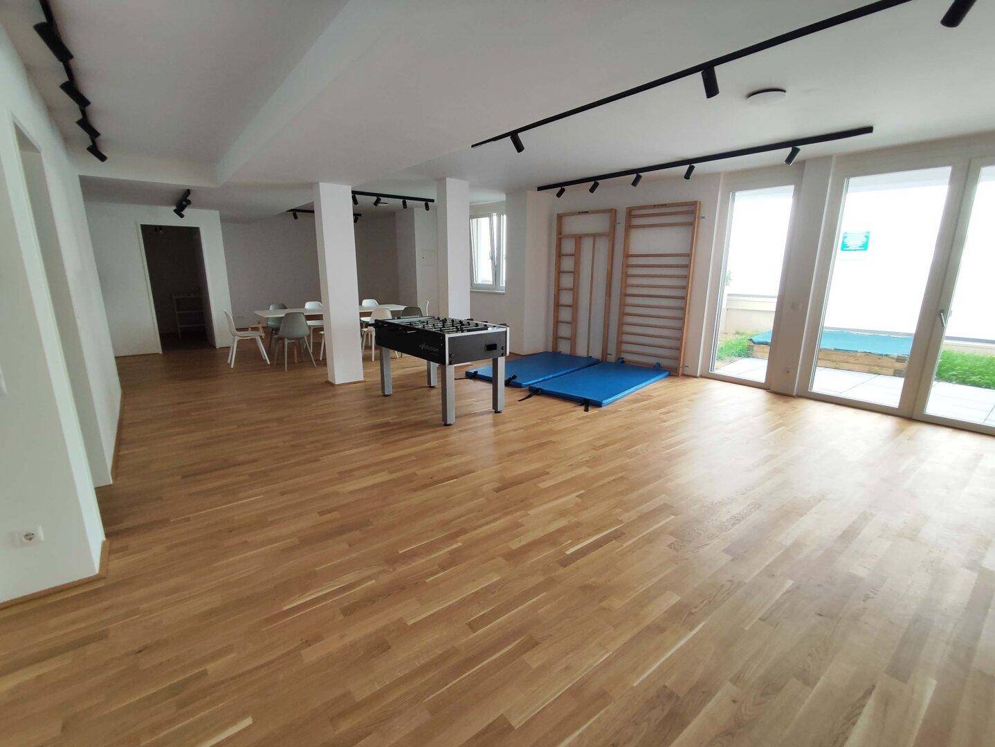 Großer Gemeinschaftsraum mit Holzboden, Tischfußball und Sprossenwänden, ideal für Freizeitaktivitäten.