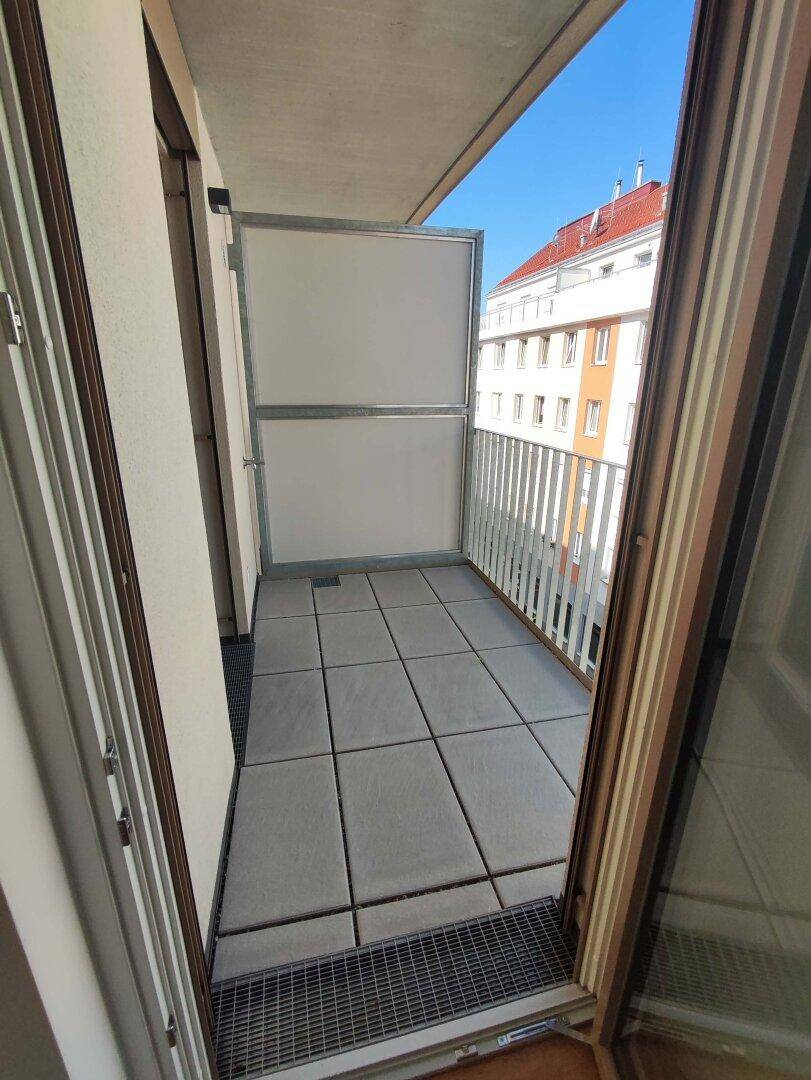 Kleiner Balkon mit grauen Fliesen und Blick auf die umliegenden Gebäude der Stadt.