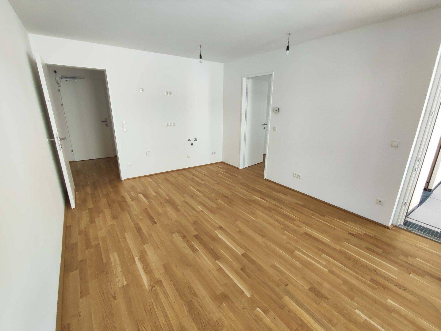 Geräumiger, unmöblierter Raum mit hellem Parkettboden und mehreren Türen zu anderen Bereichen.
